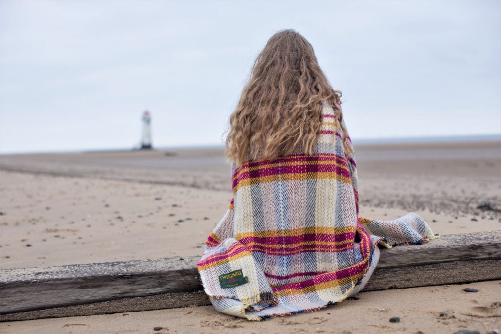 tweedmill textiles recycled blanket draped around a lady who is sitting on the beach